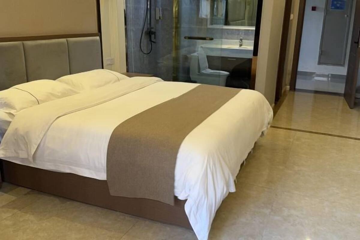 A modern hotel room with a large bed, a glass shower enclosure, and a visible bathroom with a sink and mirror.