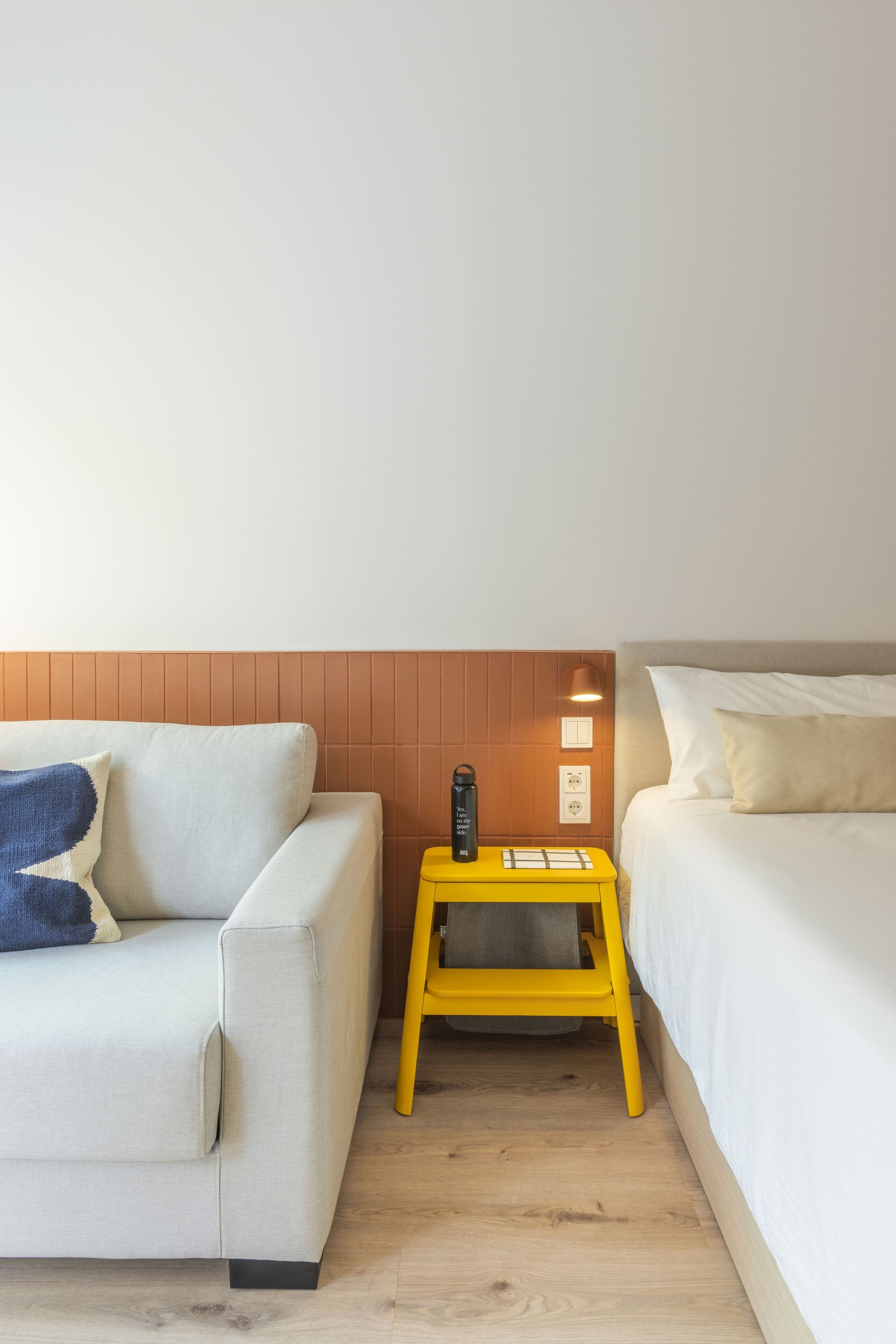 A hotel room with a sofa, a small yellow table, and a bed.
