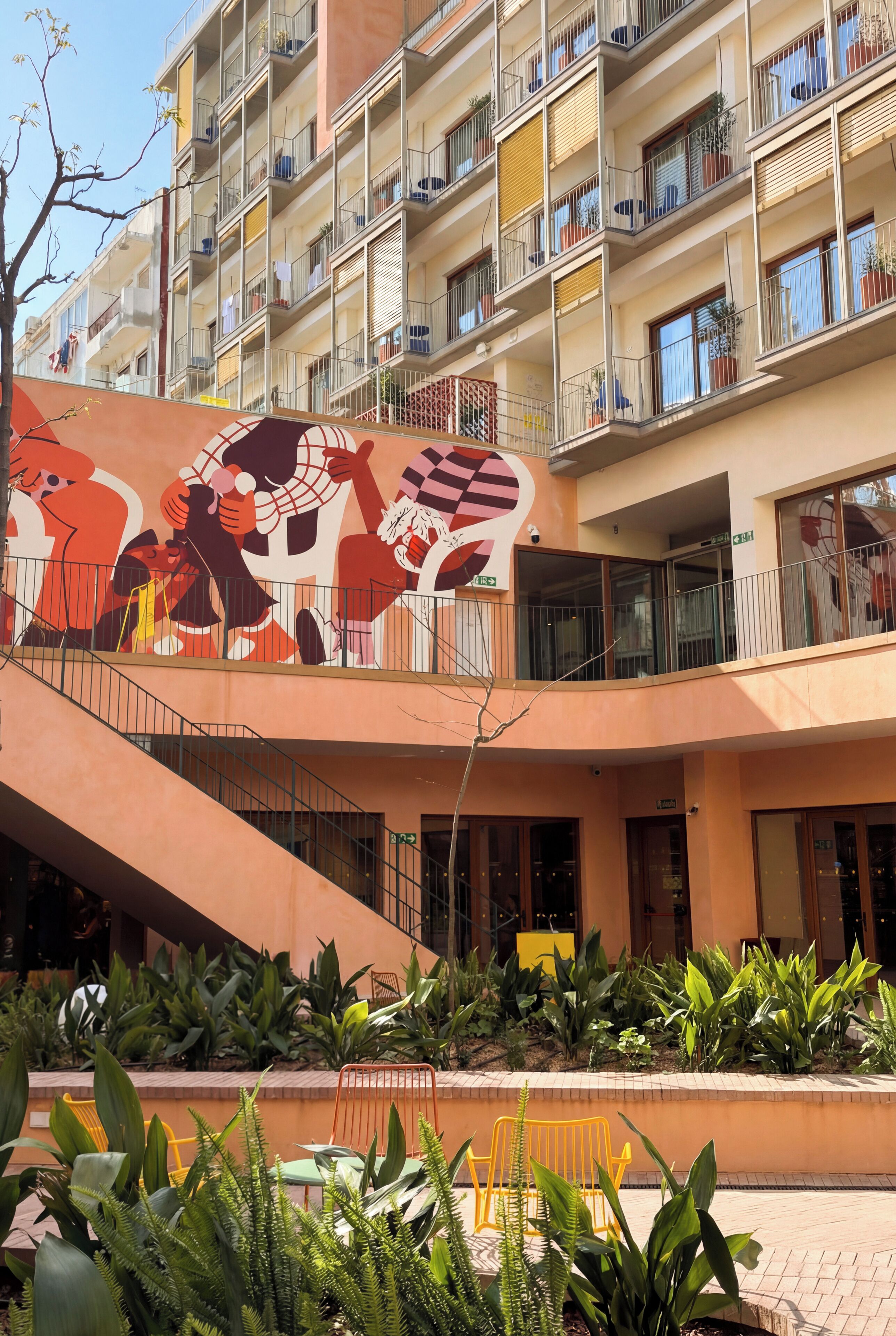 A multi-story building with balconies, a staircase, and a mural.