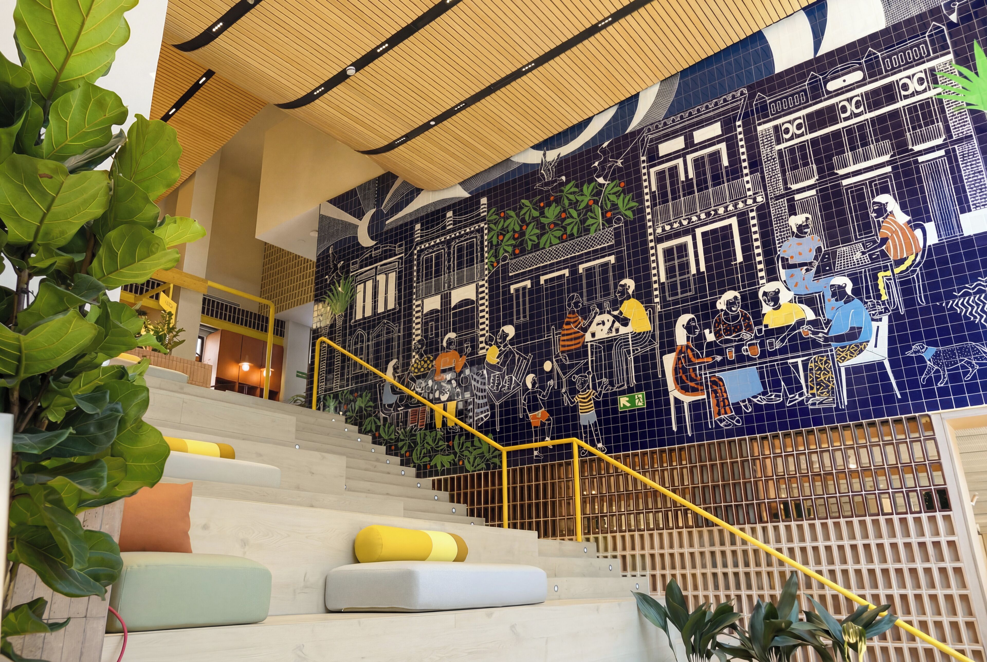 Una escalera con un mural de azulejos azules, barandilla amarilla y plantas verdes.