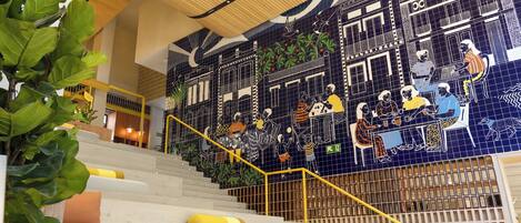Una escalera con un mural de azulejos azules, barandilla amarilla y plantas verdes.