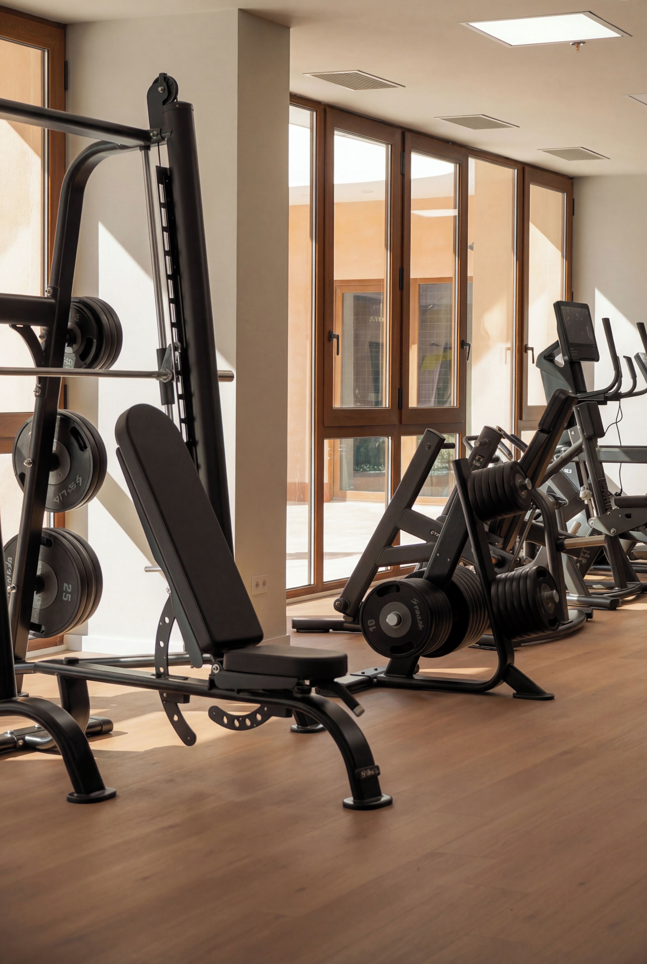 Un gimnasio con equipo de ejercicio, ventanas amplias y suelo de madera.