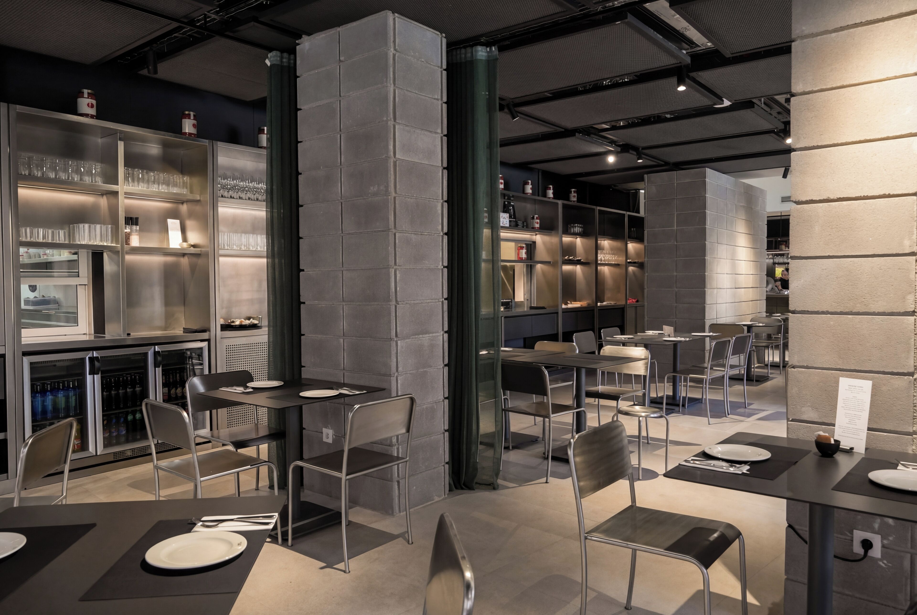 A modern restaurant interior with metal chairs, tables, and shelves with glassware.