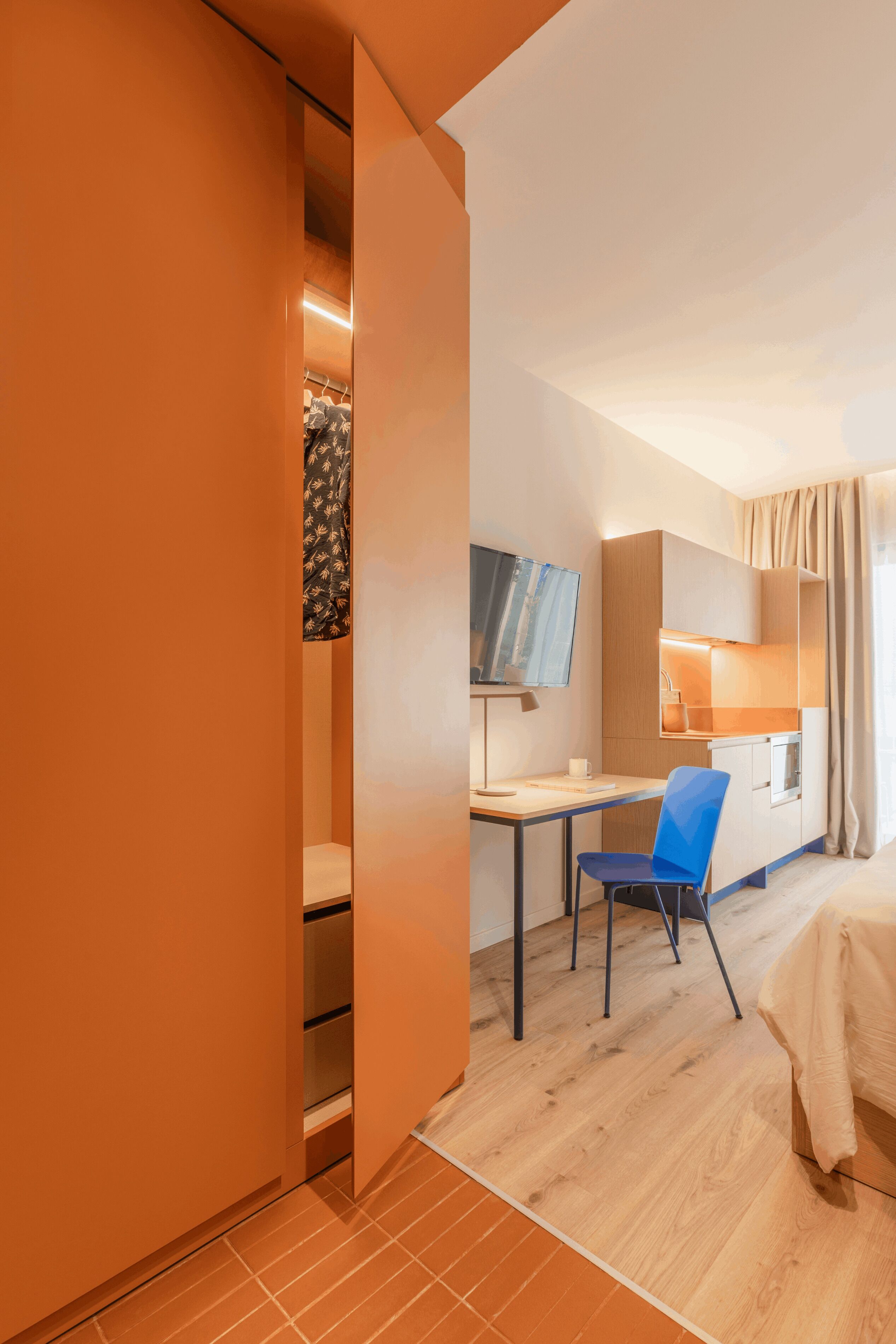 Une chambre d’hôtel moderne avec un plancher en bois, un bureau avec une chaise, un lit, une télévision et une armoire.