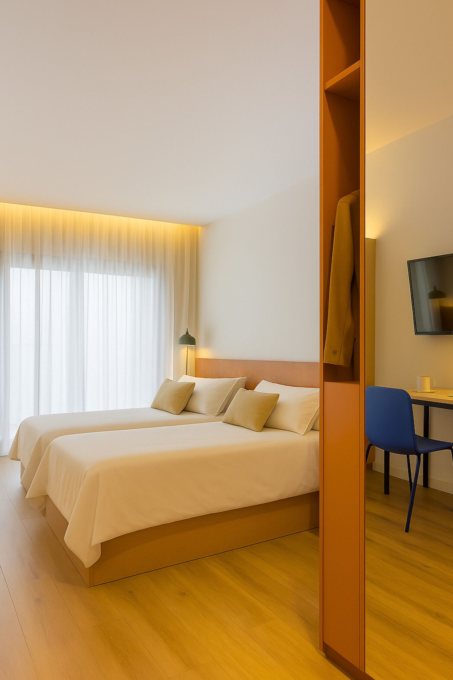 A hotel room with two beds, a desk, a chair, and a TV on the wall.