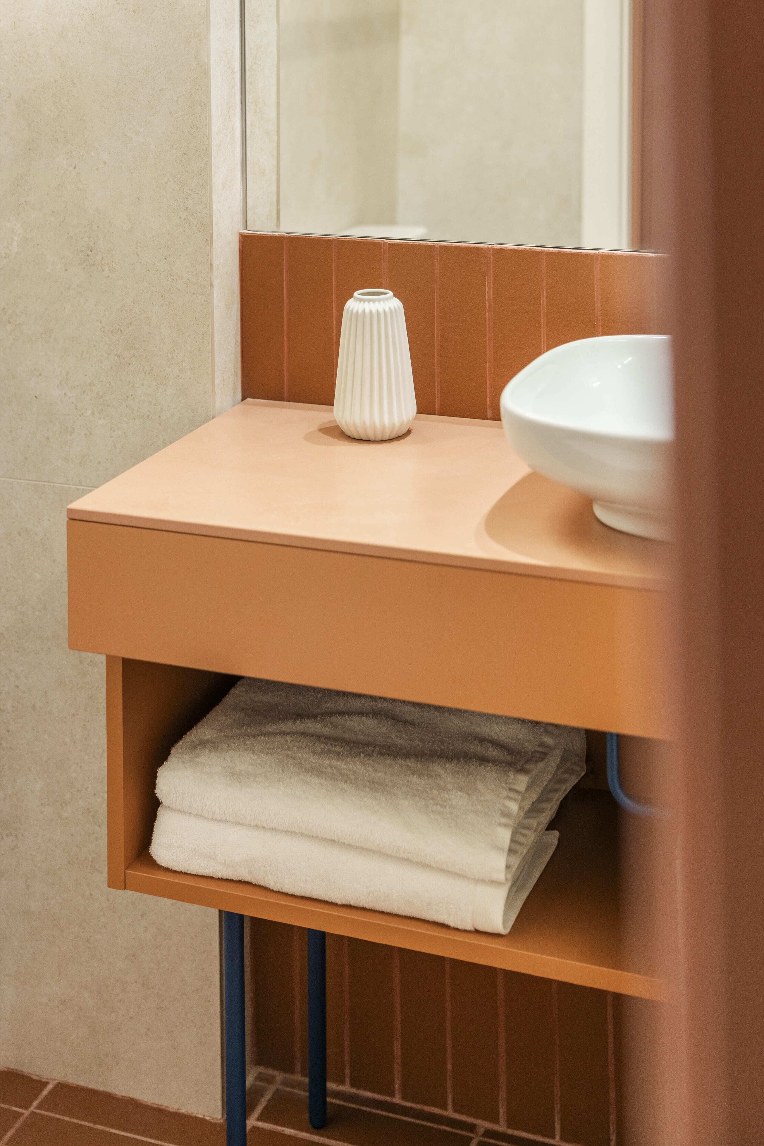 Une salle de bain avec un comptoir beige, un vase blanc et un lavabo blanc.