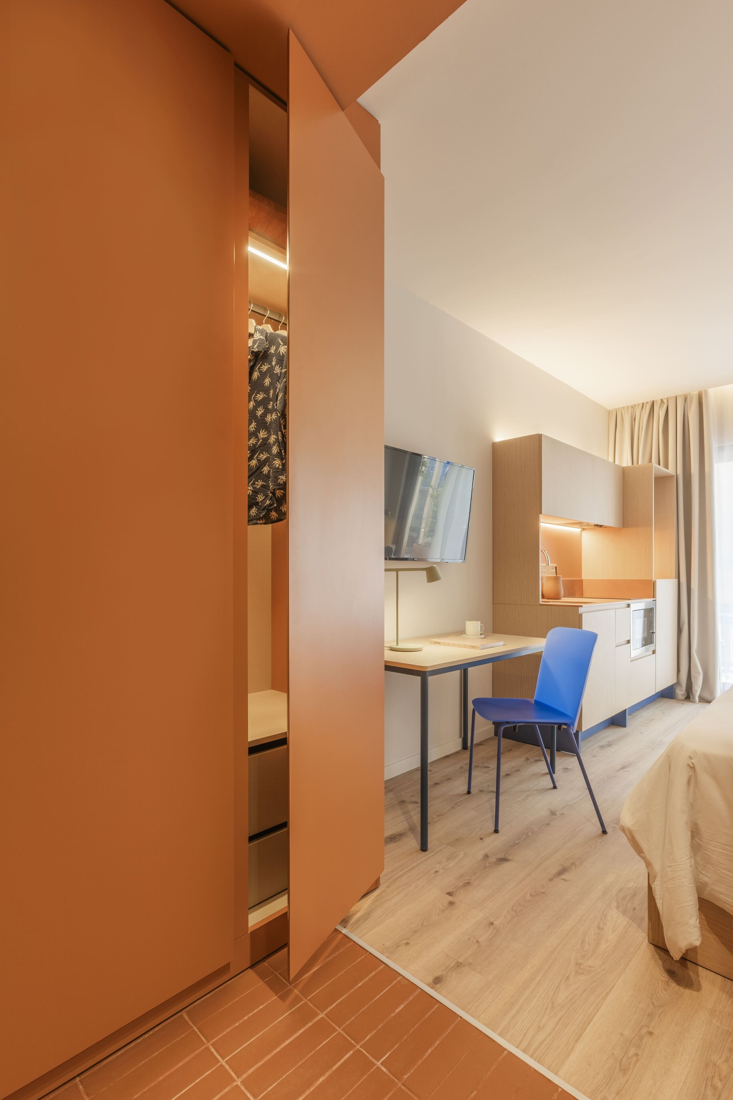 Una habitación de hotel con cama, escritorio, silla, televisor y armario.