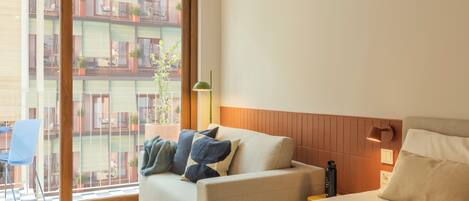 Habitación de hotel con cama, sofá, ventana y vista a balcones, además de una lámpara fijada a la pared.