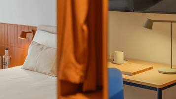 Una habitación de hotel con una cama, un escritorio con lámpara, una taza y un libro.