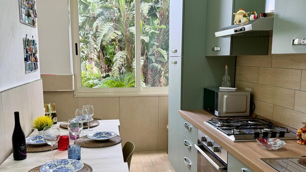 A modern kitchen with a dining area, featuring a window with a view of greenery, a microwave, stove, and cabinets. - Marianna 's House newly renovated apartment in Naples near airport (Napoli)