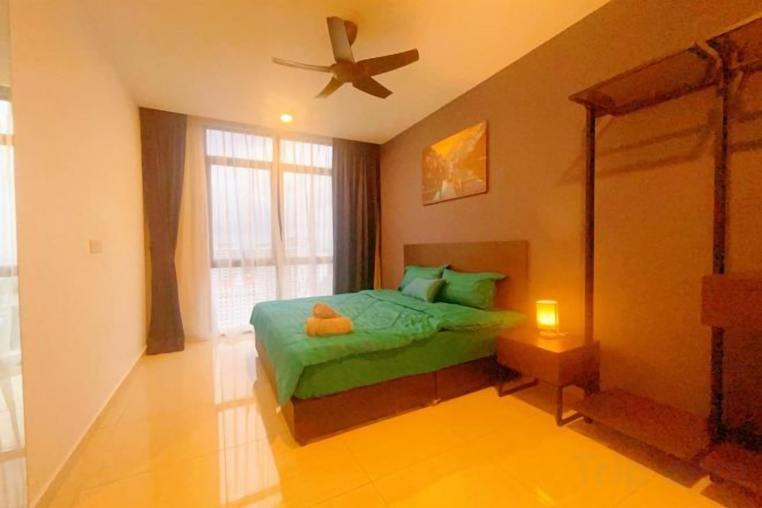 A bedroom with a bed, a ceiling fan, a nightstand with a lamp, and a window with curtains.