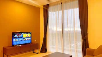 A living room with a flat-screen TV on a stand, a sofa, a coffee table, and a large window with curtains.