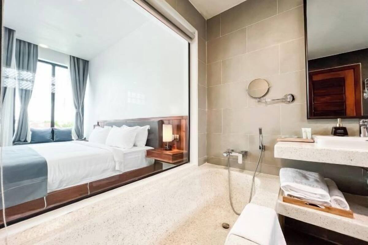Une chambre d’hôtel comprenant un lit, une table de chevet, une lampe, une douche et un meuble-lavabo dans la salle de bain avec des serviettes.