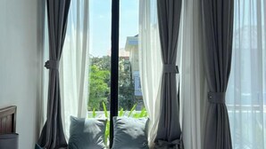 A room with a large window, grey curtains, and a view of greenery outside.