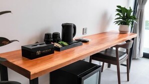 A modern room with a wooden table, a black coffee maker, a box labeled 'Emerald,' and a small refrigerator.