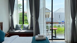 A hotel room with a bed, a window with curtains, a view of a balcony, and a small table.