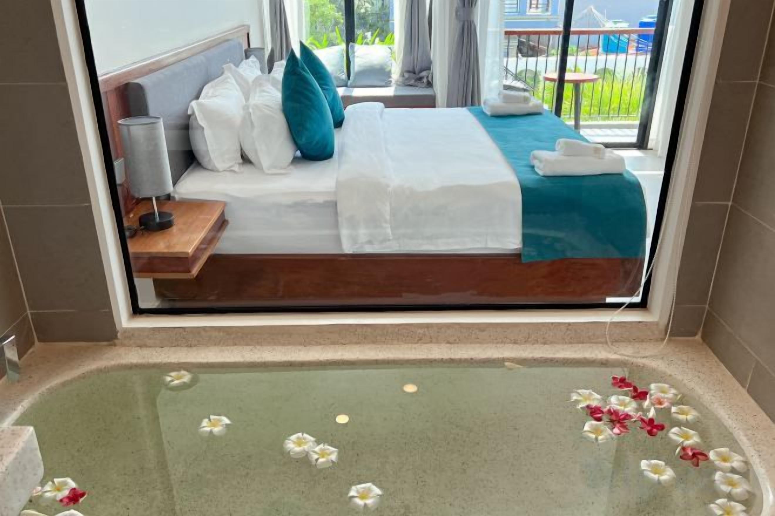 Et hotelværelse med en seng, et badekar med blomster og udsigt til en pool og en bygning.