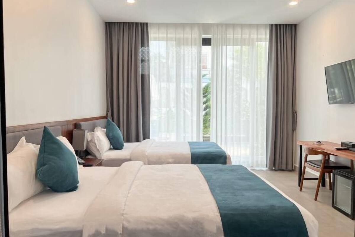 Une chambre d’hôtel avec deux lits, un bureau, une télévision et de grandes fenêtres avec des rideaux.