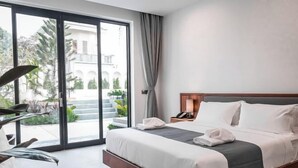A hotel room with a bed, a desk, a lamp, and a view of the outside.