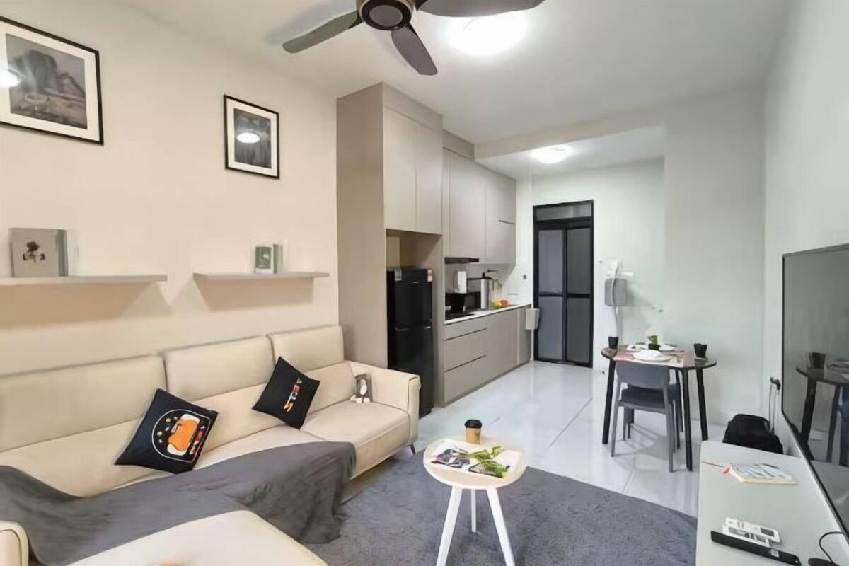 Een moderne woonkamer met een bank, salontafel en televisie. Er is een keuken met kasten en een koelkast.