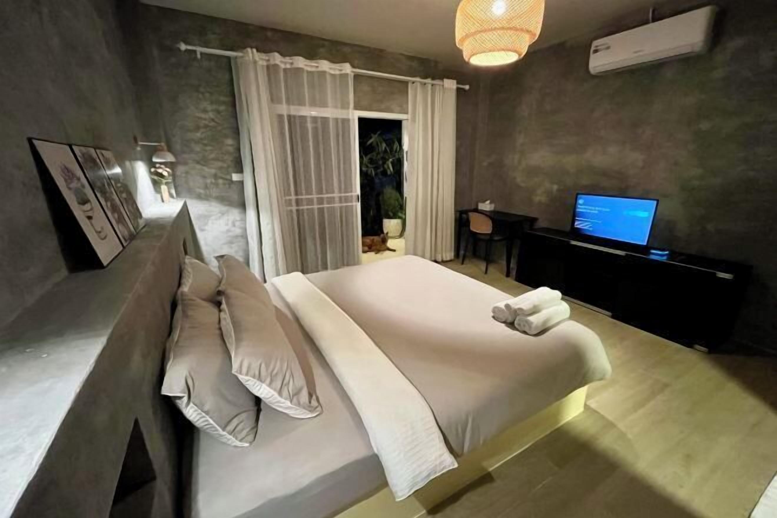 Un dormitorio moderno con una cama grande, un escritorio con ordenador y vistas al exterior.