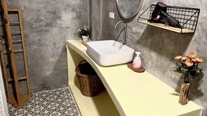 A bathroom with a white sink, a mirror, a shelf with a hairdryer, a small plant, and a vase with flowers. - The Summer Cottage (Koh Chang)