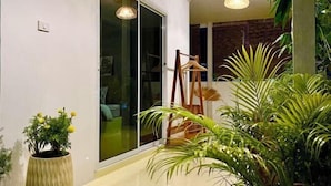 A modern interior with a sliding glass door leading to a balcony, a hanging light fixture, and indoor plants. - The Summer Cottage (Koh Chang)