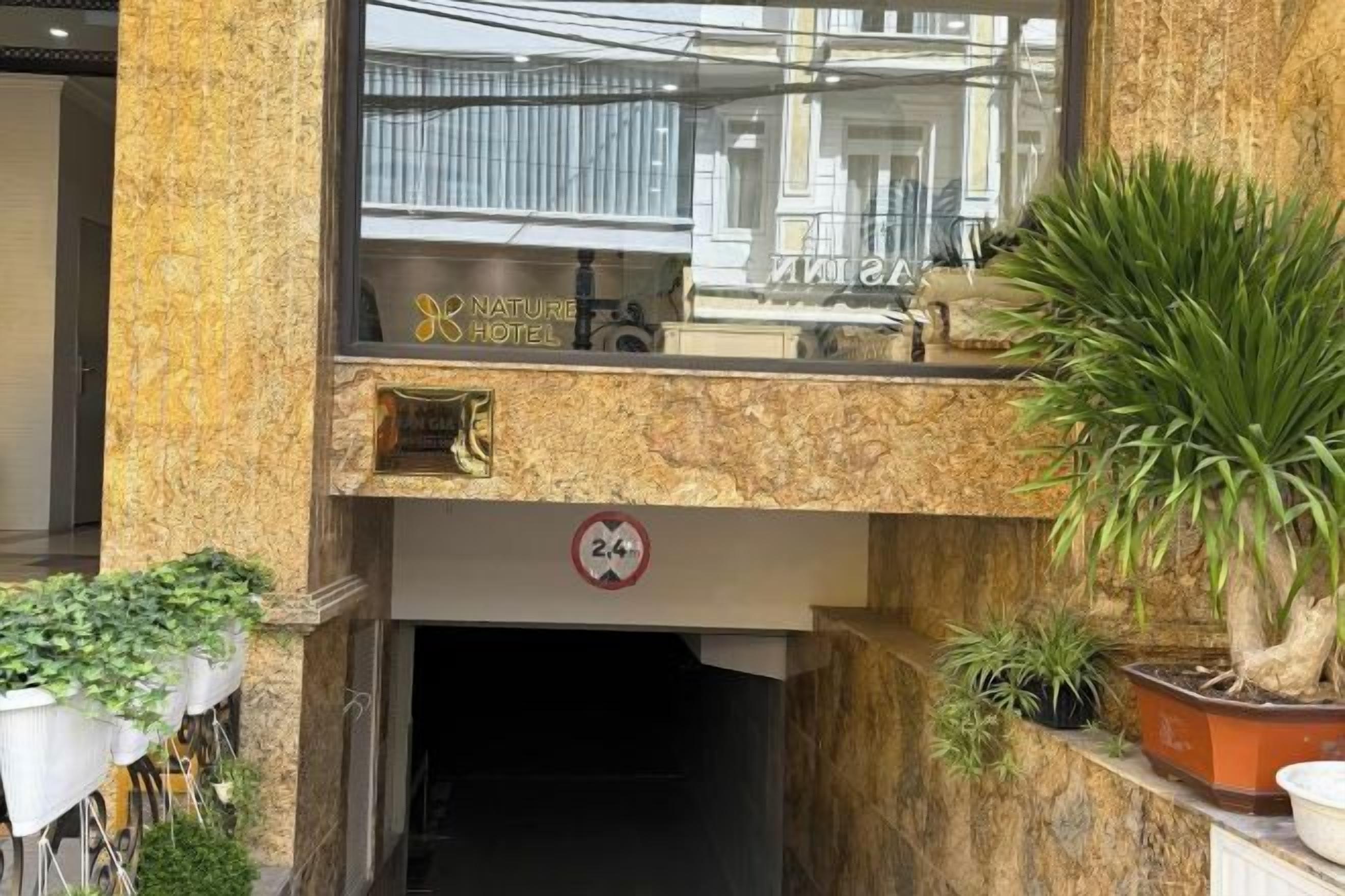 A hotel entrance with a reception desk, a sign for the hotel, and potted plants.