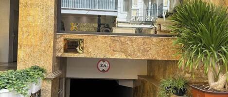 A hotel entrance with a reception desk, a sign for the hotel, and potted plants.