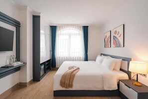 Une chambre d’hôtel moderne, dotée d’un grand lit, d’une table de chevet avec une lampe, d’un téléviseur à écran plat fixé au mur et d’une fenêtre avec des rideaux.