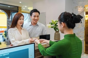 A reception desk with a computer monitor, a plant, and a vase. - Nature Hotel - Le Dai Hanh (Dalat)