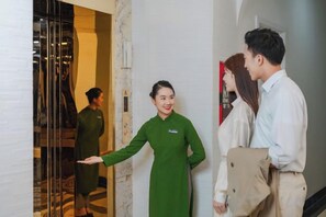 A hotel reception area with a reception desk, a fire extinguisher, and a glass door leading to a room. - Nature Hotel - Le Dai Hanh (Dalat)