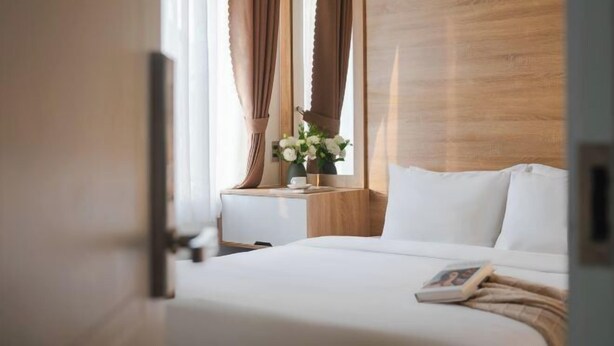 A hotel room with a wooden headboard, a bedside table with a vase of flowers, and a bed with white linens. - Nature Hotel - Le Dai Hanh (Dalat)