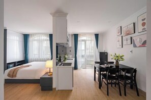 Une chambre d’hôtel de taille réduite, comprenant un lit, une table de chevet, une lampe et une petite kitchenette.