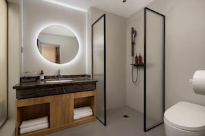 A modern bathroom with a wooden vanity, a round mirror, a shower enclosure, and a toilet.