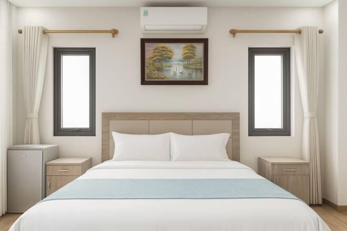 A hotel room with a bed, two bedside tables, a nightstand, a small cabinet, and a painting on the wall.