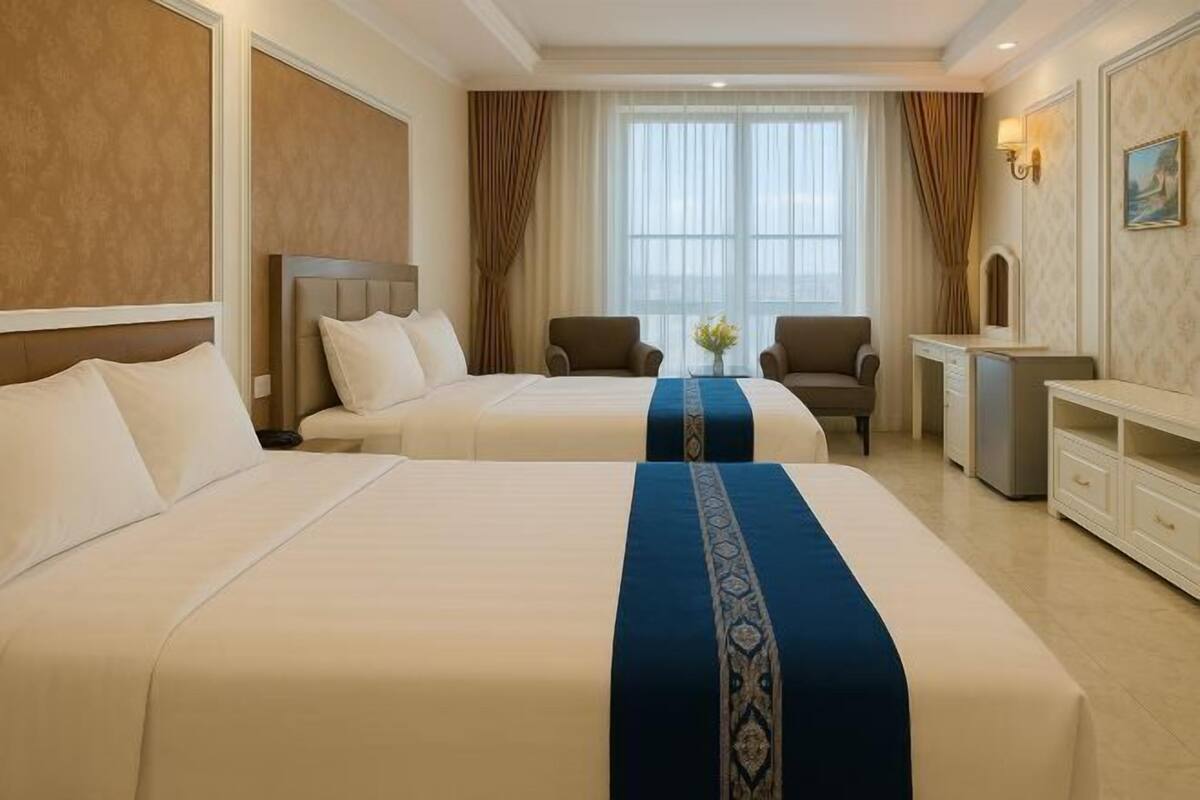 A hotel room with two beds, a desk, a chair, and a large window with curtains.