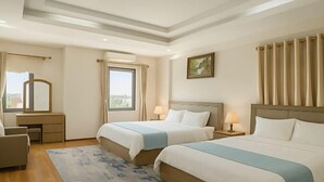 A hotel room with two beds, a desk, a chair, a window with curtains, and a painting on the wall. - XIAN HOTEL (The Grand Hotel) (Bac Ninh)