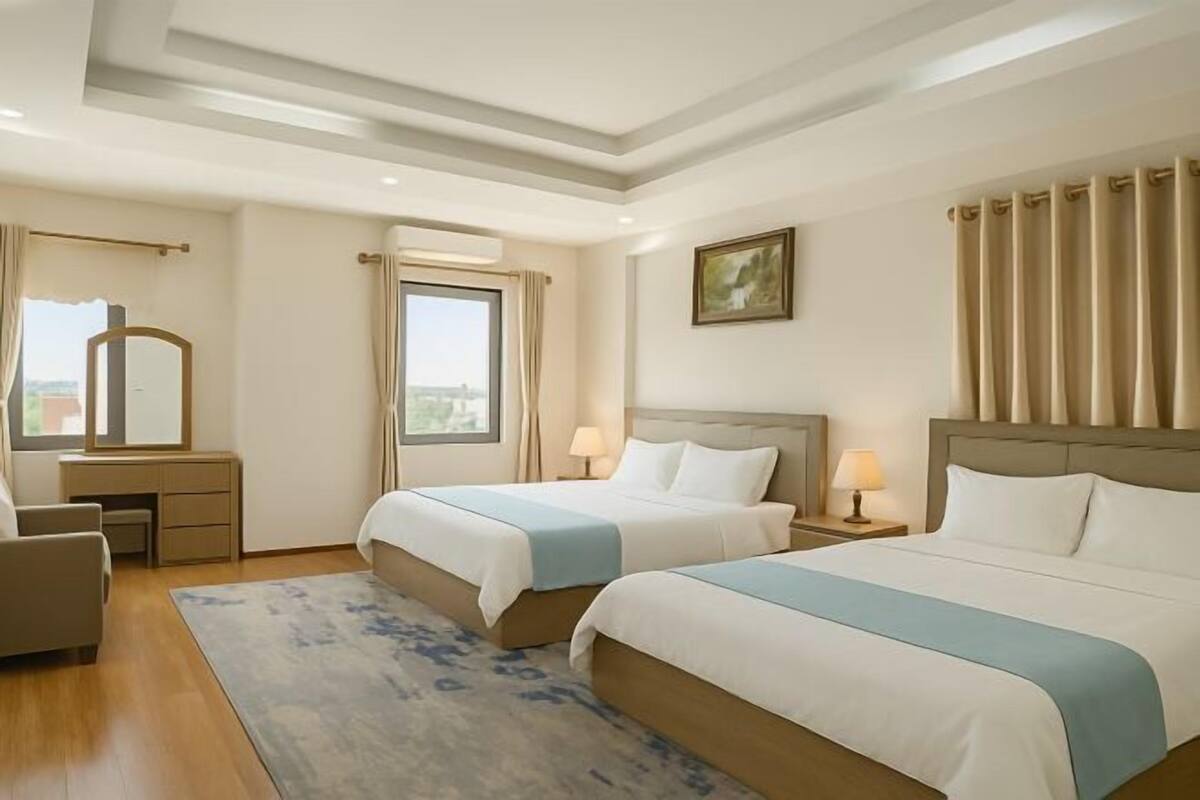A hotel room with two beds, a desk, a chair, a window with curtains, and a painting on the wall.