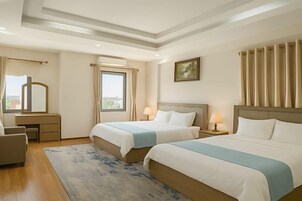 Habitación de hotel con dos camas, un escritorio, una silla, un ventanal con cortinas y un cuadro en la pared.