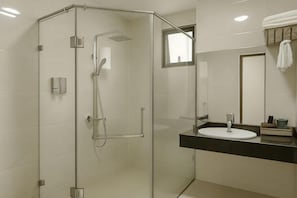 A glass-enclosed shower with a handheld showerhead, a sink with a mirror, and a towel rack. - XIAN HOTEL (The Grand Hotel) (Bac Ninh)