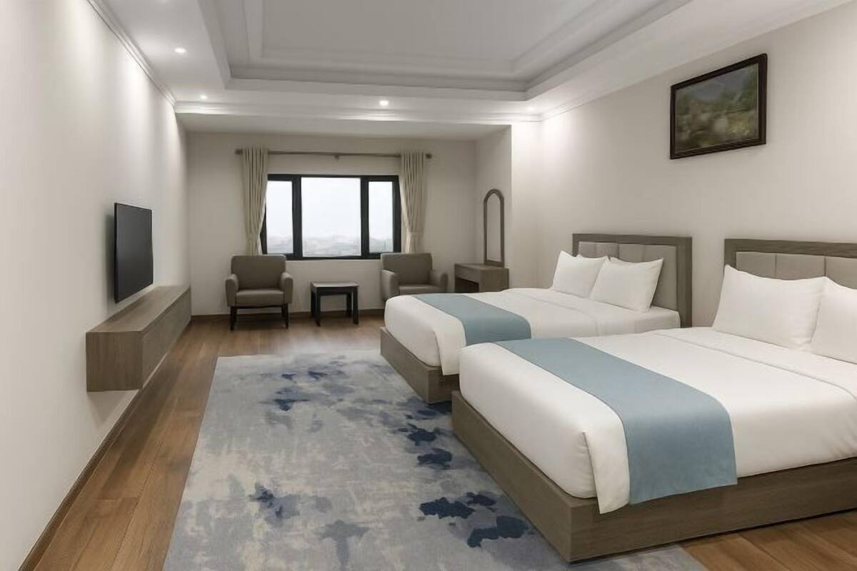 A hotel room with two beds, a TV, a small table, a chair, and a window with curtains.