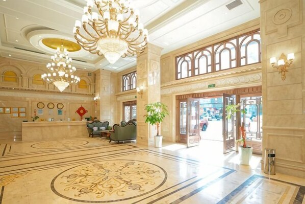 A spacious lobby with a grand chandelier, a reception desk, and a large, ornate carpet.