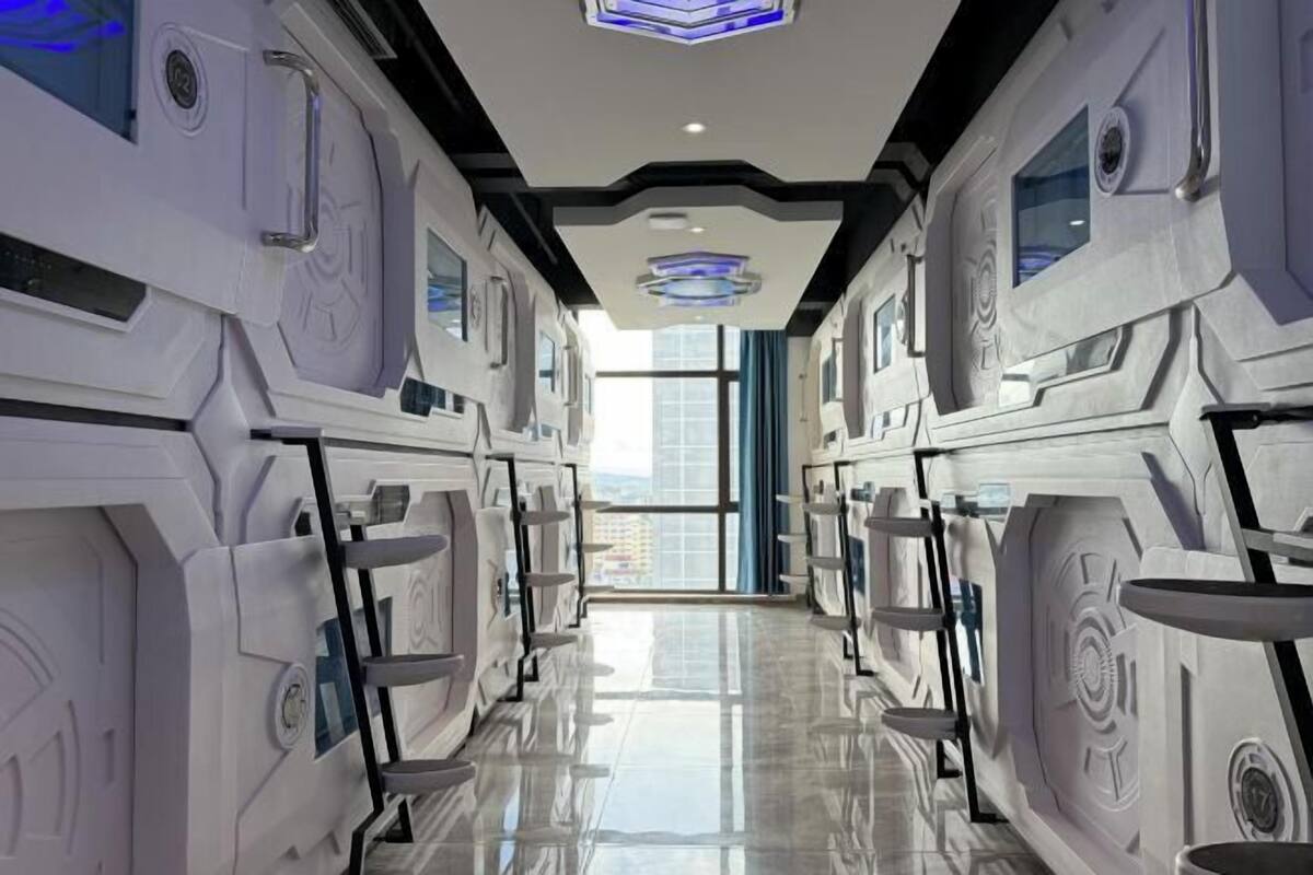 A futuristic hotel corridor with a reflective floor, symmetrical design, and large windows.