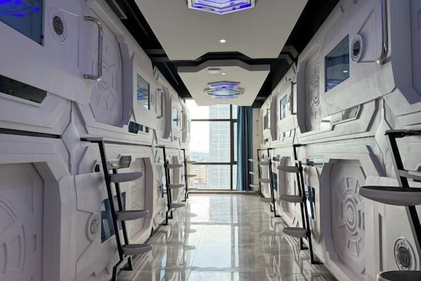 Un couloir d’hôtel futuriste avec un sol réfléchissant, une conception symétrique et de grandes fenêtres.