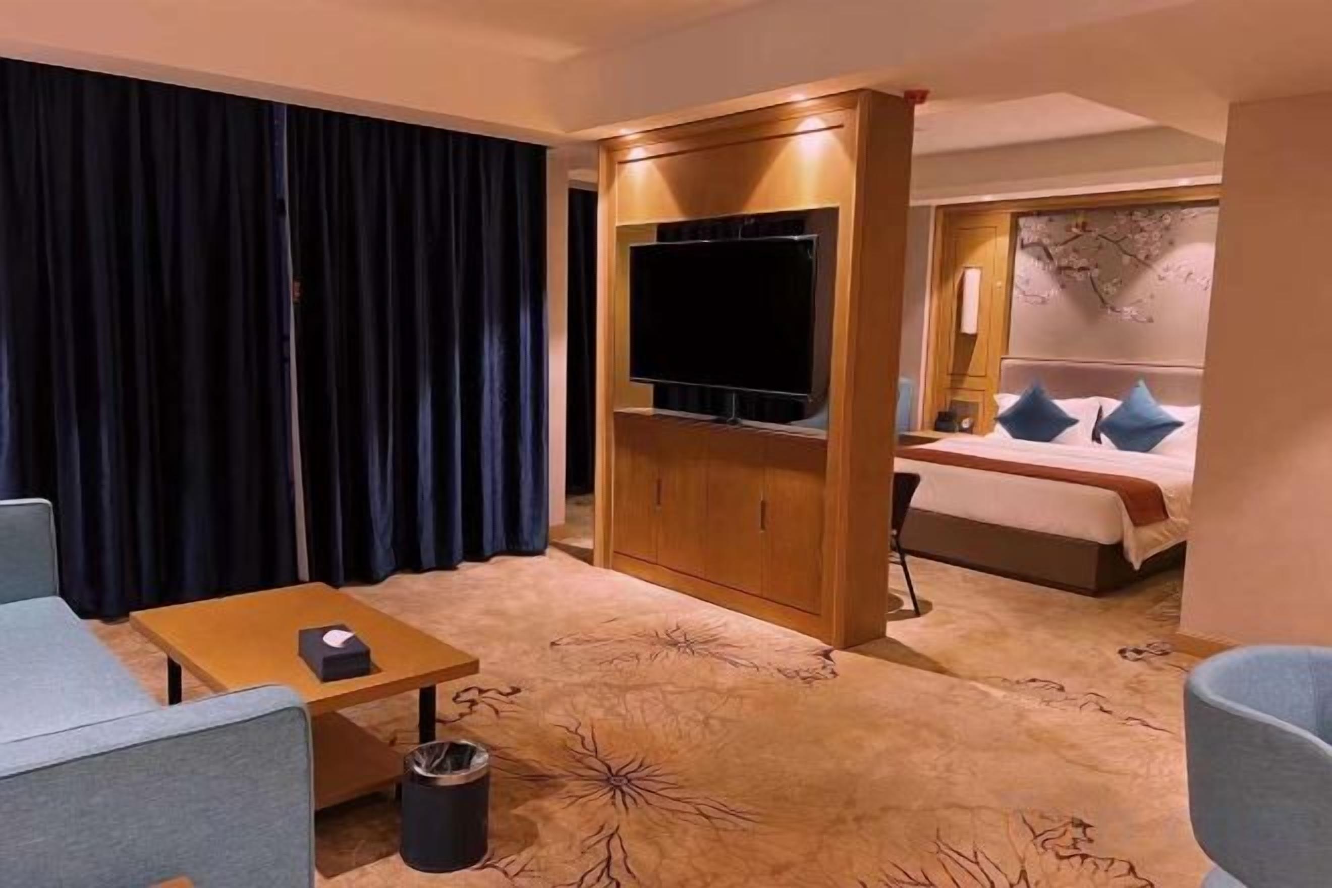 Ein Hotelzimmer mit Sofa, Fernseher, Bett mit Kissen und Teppich mit Blumenmuster.