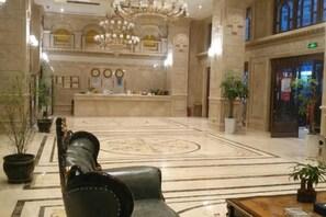 A lobby with a reception desk, a chandelier, and a large, ornate carpet.