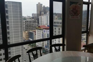 A room with a large window offering a view of a cityscape, a round table, and two chairs.