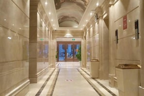 A marble-floored corridor with columns, a reception desk, and a door leading to a room.