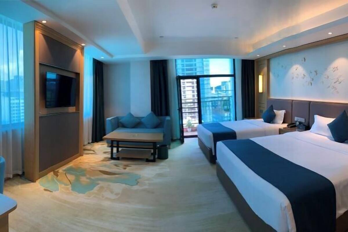 A hotel room with two beds, a TV, a sofa, and a view of the city.